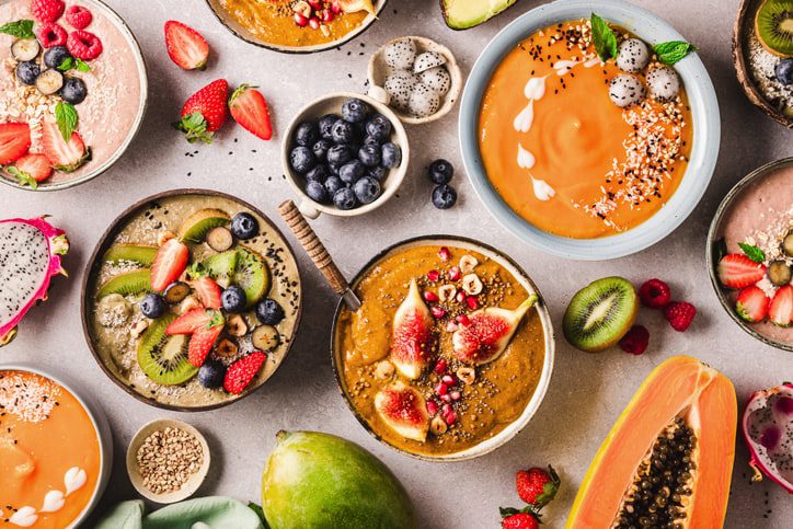colourful smoothie bowls surrounded by fresh fruits