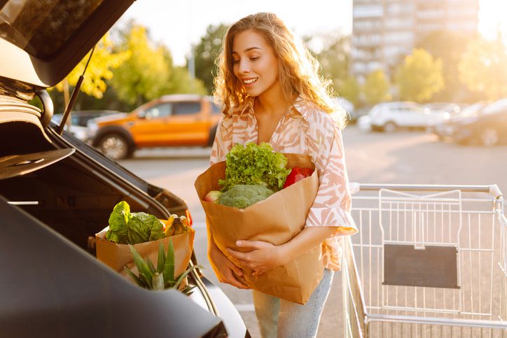Young woman putting groceries in a paper bag in the trunk of her car.